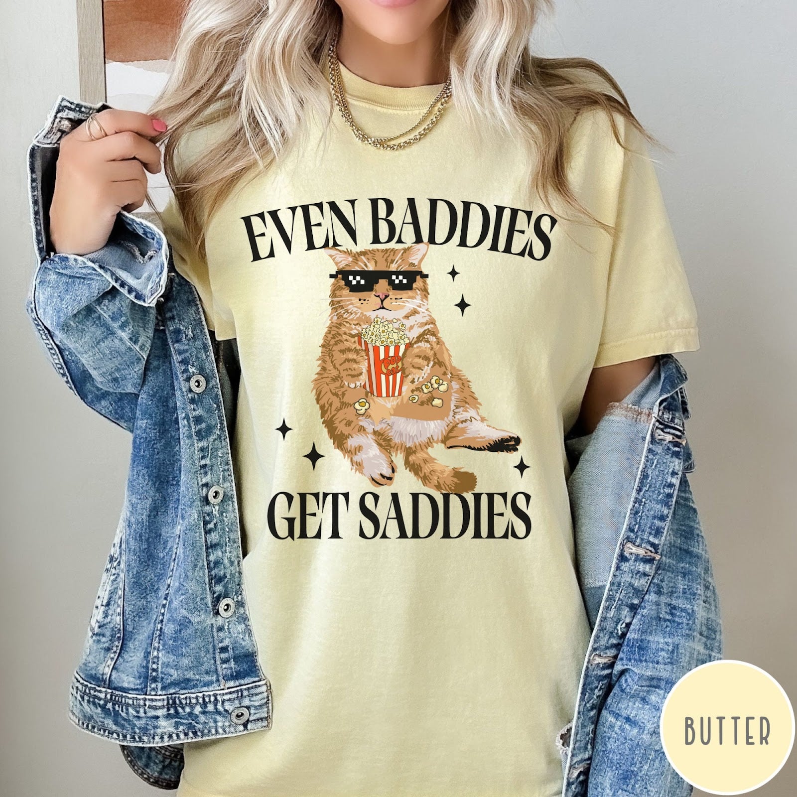 Comfort Colors tee in Butter featuring cat graphic with sunglasses and popcorn, text Even Baddies Get Saddies