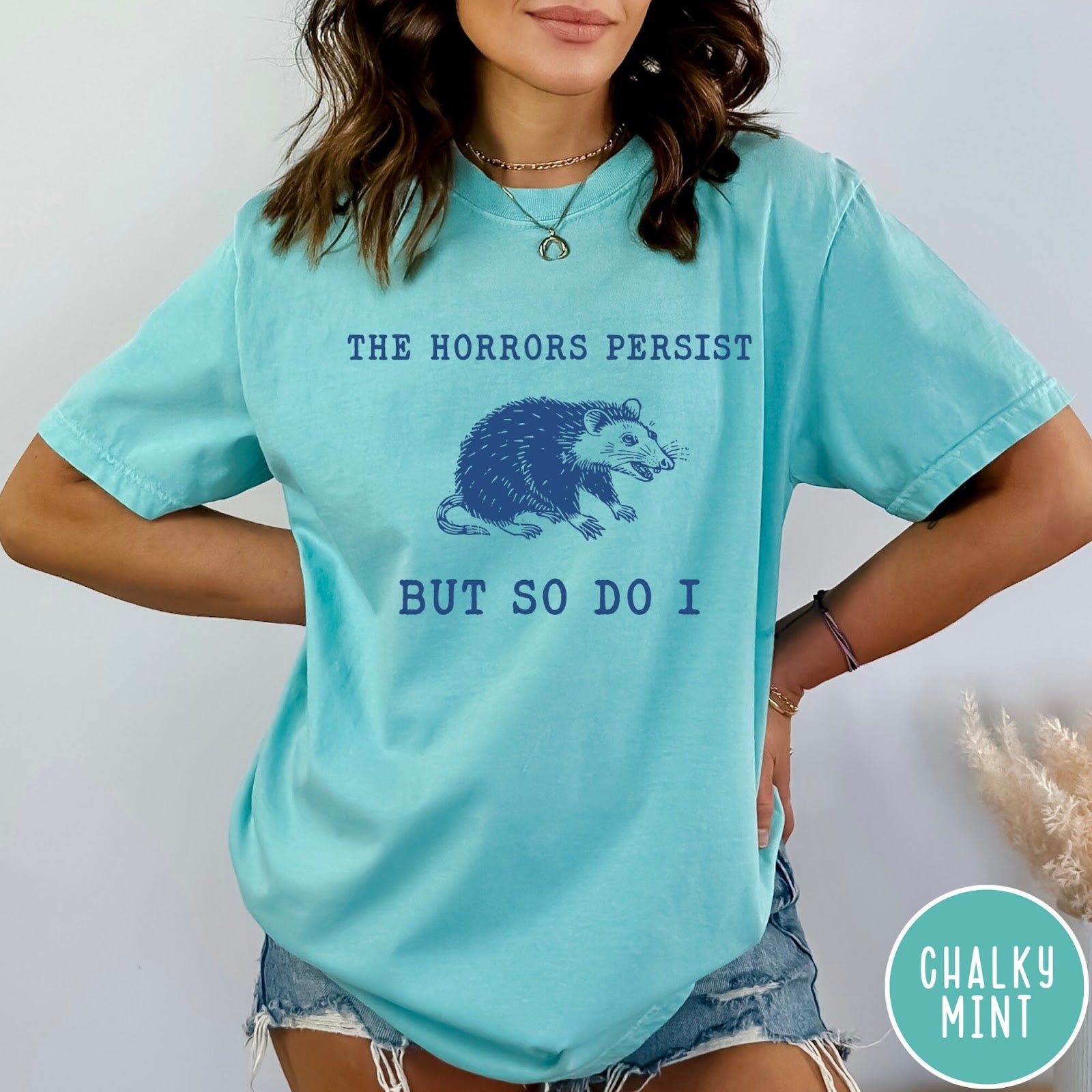 Comfort Colors tee in Chalky Mint featuring illustrative style opossum graphic with text The Horrors Persist But So Do I