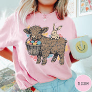 Comfort Colors tee in Blossom featuring graphic style Highland cow and bunny with an Easter egg basket