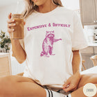Comfort Colors tee in Ivory featuring vintage style graphic of a standing raccoon with text Expensive and Difficult