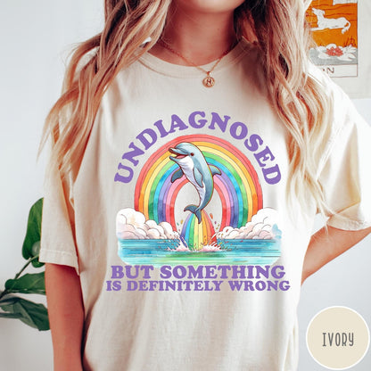 Comfort Colors tee in Ivory featuring graphic style illustration of a dolphin jumping through a colorful rainbow
