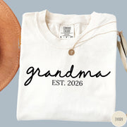Comfort Colors tee in Ivory featuring cursive Grandma Est 2026 text in a clean black graphic style