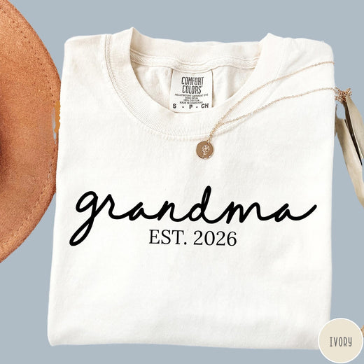 Comfort Colors tee in Ivory featuring cursive Grandma Est 2026 text in a clean black graphic style
