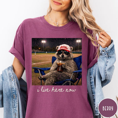 Comfort Colors tee in Berry featuring graphic raccoon wearing sunglasses and baseball cap sitting in camping chair