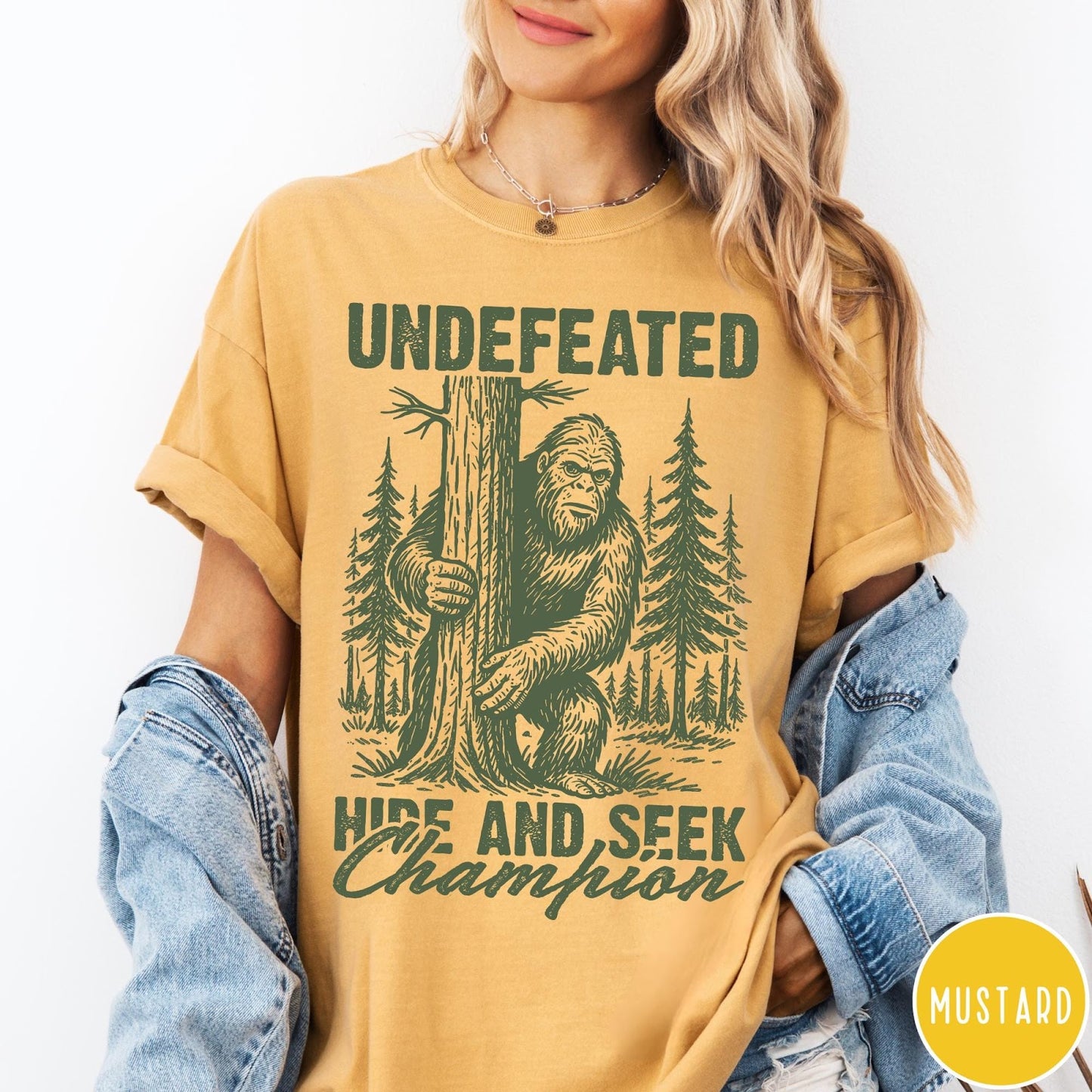 Comfort Colors tee in Mustard featuring vintage style Bigfoot graphic hiding behind a tree in the forest