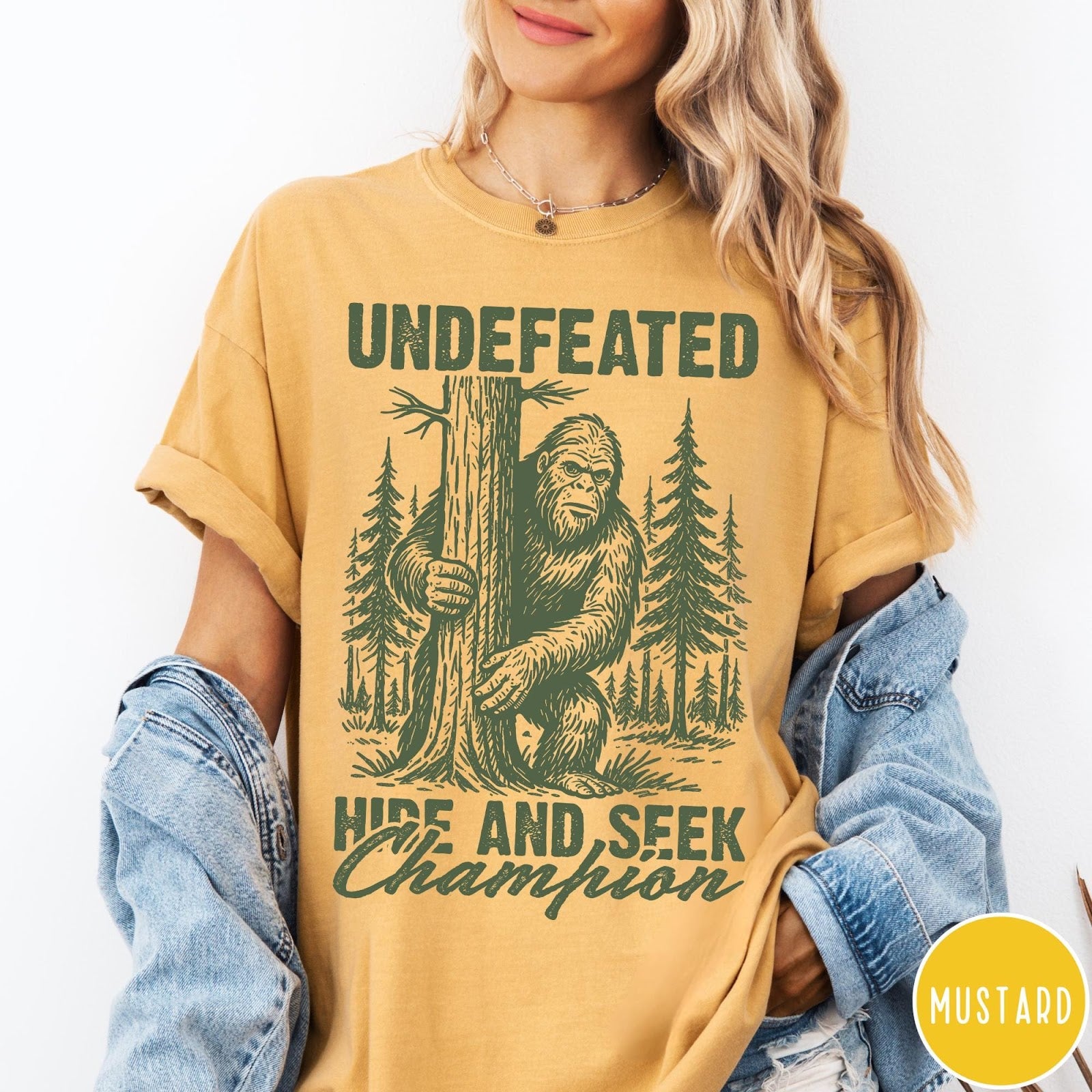 Comfort Colors tee in Mustard featuring vintage style Bigfoot graphic hiding behind a tree in the forest