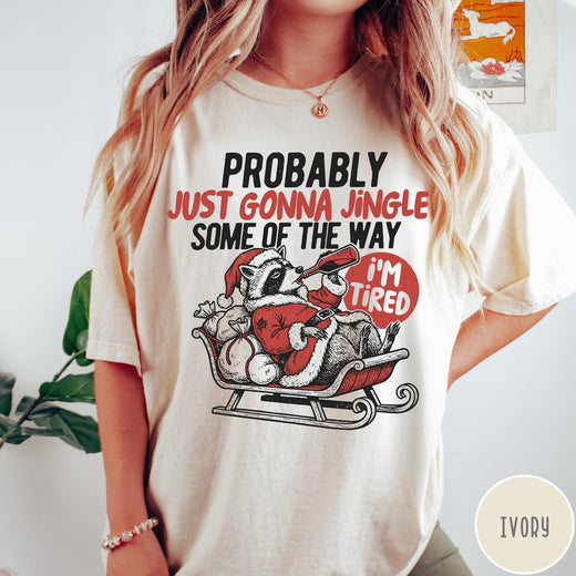 Comfort Colors tee in Ivory featuring vintage style graphic of a tired raccoon in a Santa sleigh