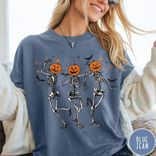 Comfort Colors tee in Blue Jean featuring dancing skeleton graphic with jack-o'-lantern heads and small orange stars