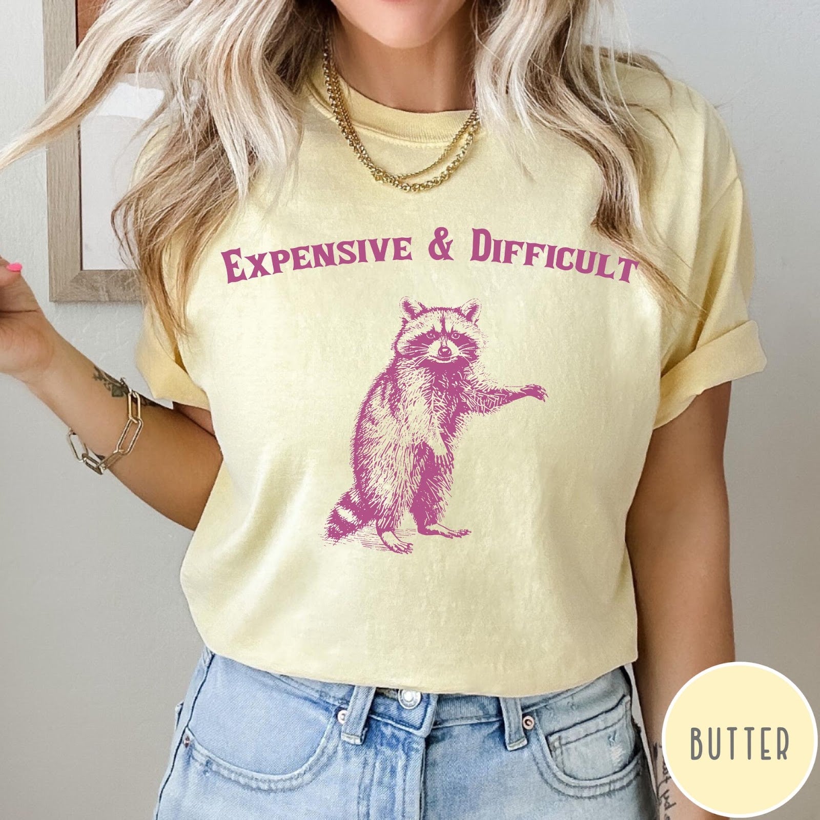 Comfort Colors tee in Butter featuring vintage style graphic of a standing raccoon with text Expensive and Difficult