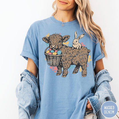 Comfort Colors tee in Washed Denim featuring graphic style illustration of a Highland cow with bunny and eggs