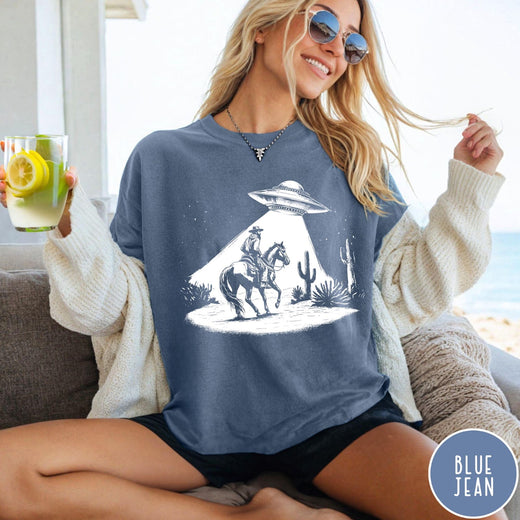 Comfort Colors tee in Blue Jean featuring western graphic style cowboy on horseback being abducted by a UFO
