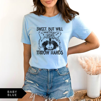 Comfort Colors tee in Baby Blue featuring graphic style raccoon illustration with text Sweet, but will throw hands