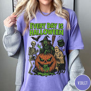 Comfort Colors tee in Violet featuring Halloween graphic with a witch, skeleton, ghost, and a dripping pumpkin.