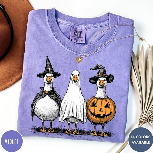 Comfort Colors tee in Violet featuring Halloween graphic with three geese dressed as a witch, ghost, and pumpkin