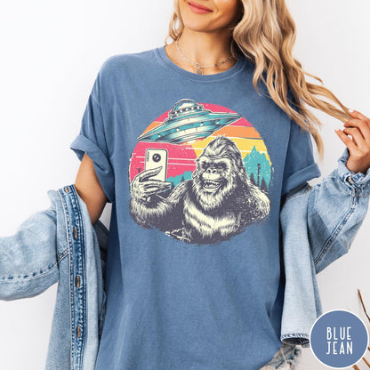 Comfort Colors tee in Blue Jean featuring retro graphic design of Bigfoot taking a selfie with a UFO