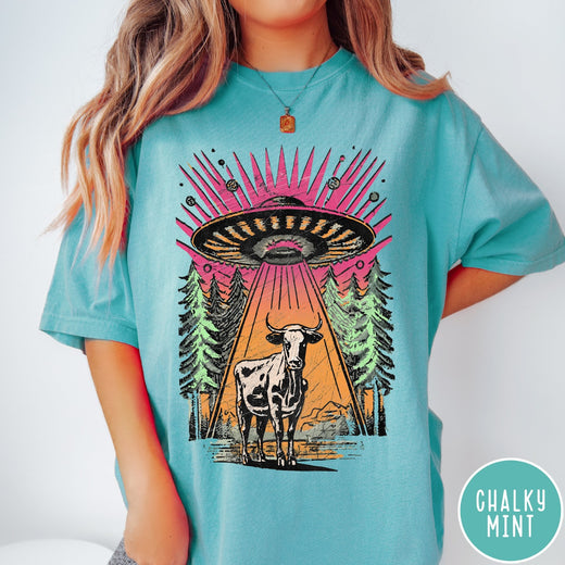 Comfort Colors tee in Chalky Mint featuring graphic style cow being abducted by a UFO in the forest