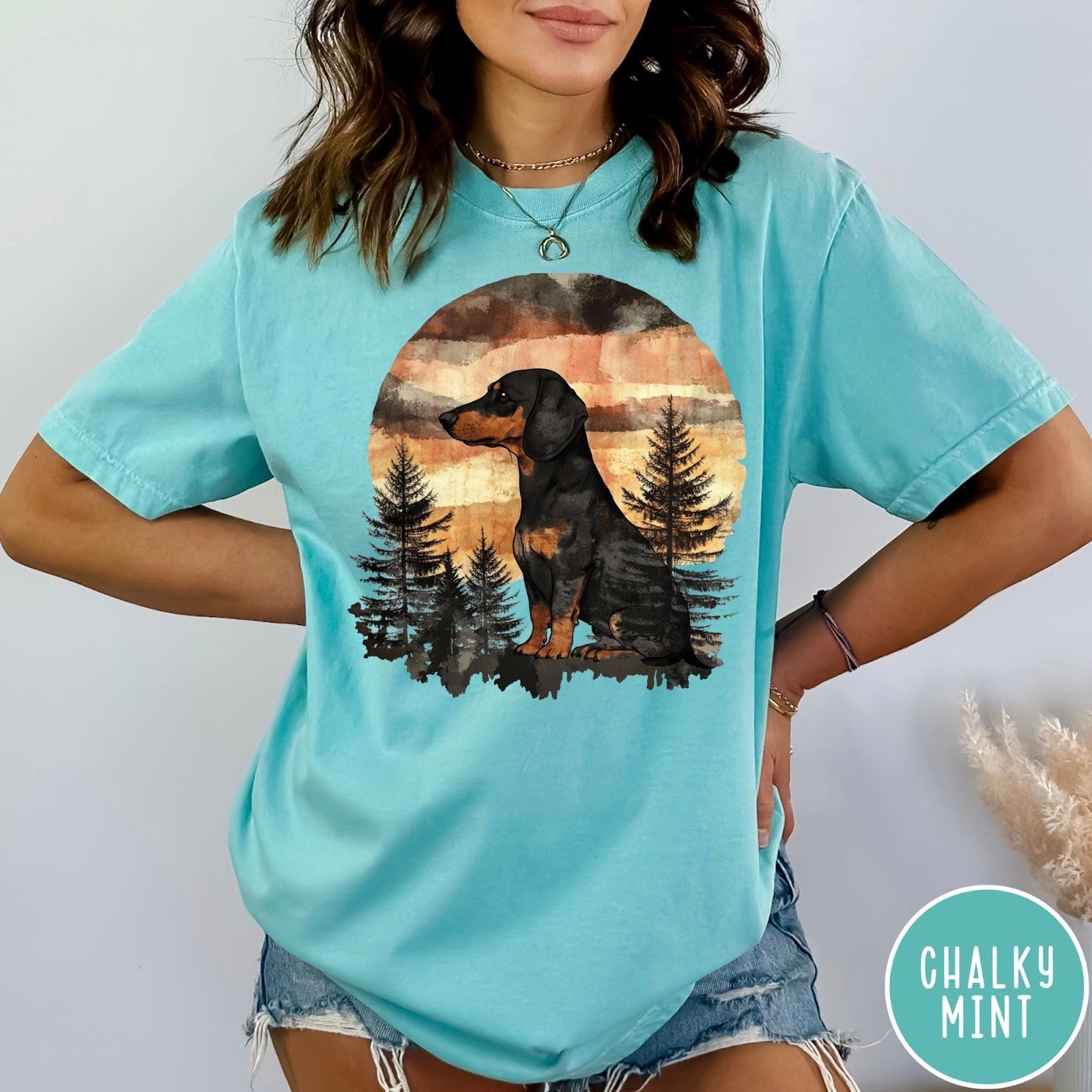 Comfort Colors tee in Chalky Mint featuring vintage style graphic of a dachshund sitting in a forest sunset