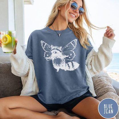 Comfort Colors tee in Blue Jean featuring whimsical graphic style of a raccoon with large detailed butterfly wings