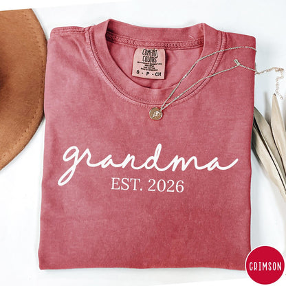 Comfort Colors tee in Crimson featuring cursive Grandma Est 2026 text in a clean white graphic style