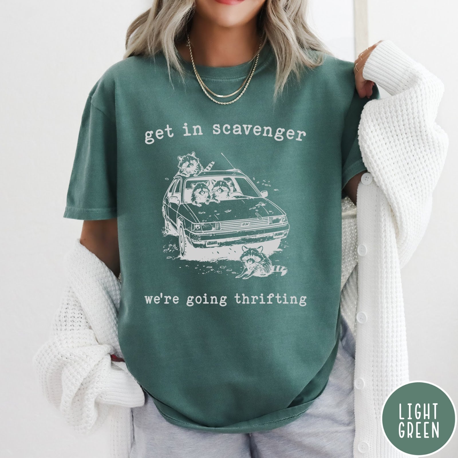 Comfort Colors tee in Light Green featuring illustrated style graphic of raccoons riding in a car and thrifting