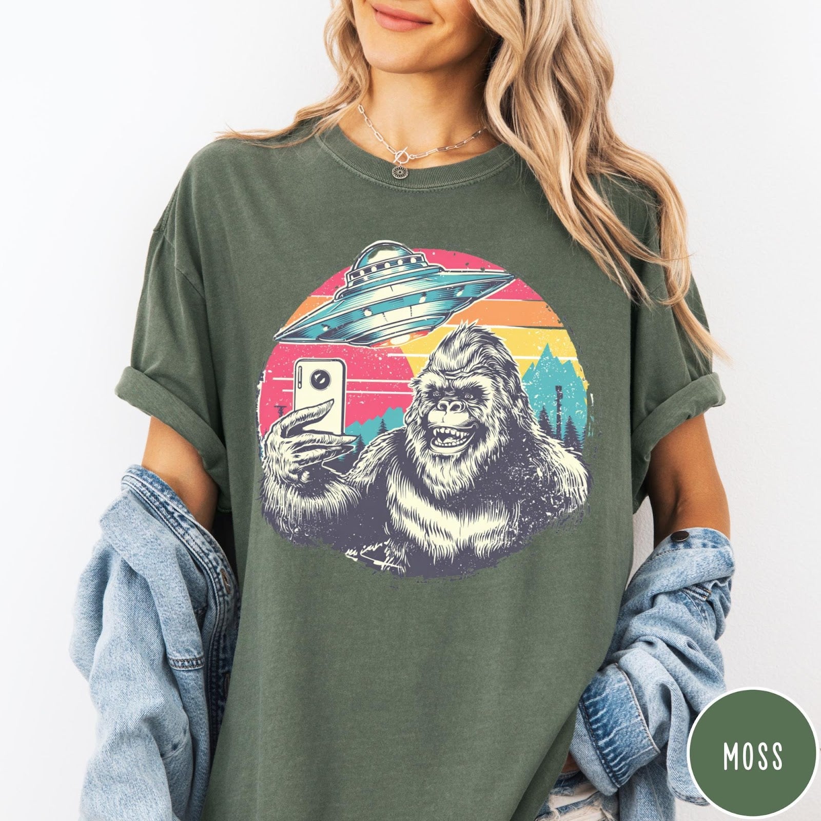 Comfort Colors tee in Moss featuring retro Bigfoot selfie graphic with a UFO and sunset mountain background