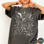 Comfort Colors tee in Pepper featuring line art graphic of various dinosaurs wearing astronaut helmets in space