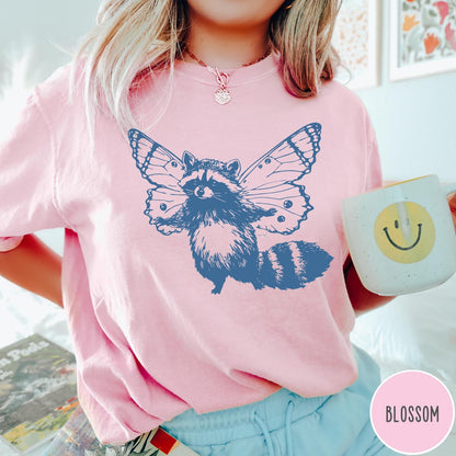 Comfort Colors tee in Blossom featuring whimsical graphic style of a raccoon with large detailed butterfly wings