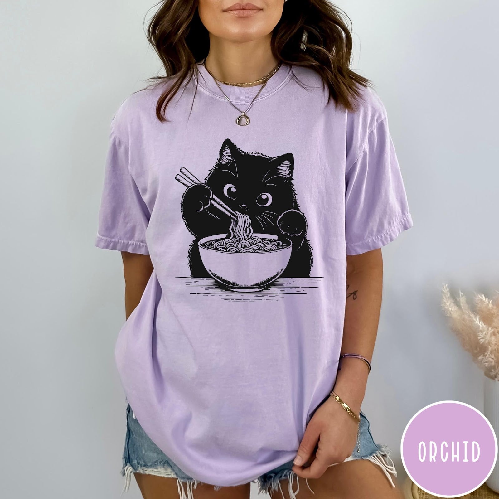 Comfort Colors tee in Orchid featuring graphic illustration of a cute black cat eating a bowl of ramen