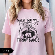 Comfort Colors tee in Pink featuring graphic style raccoon illustration with text Sweet, but will throw hands