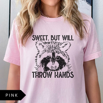 Comfort Colors tee in Pink featuring graphic style raccoon illustration with text Sweet, but will throw hands