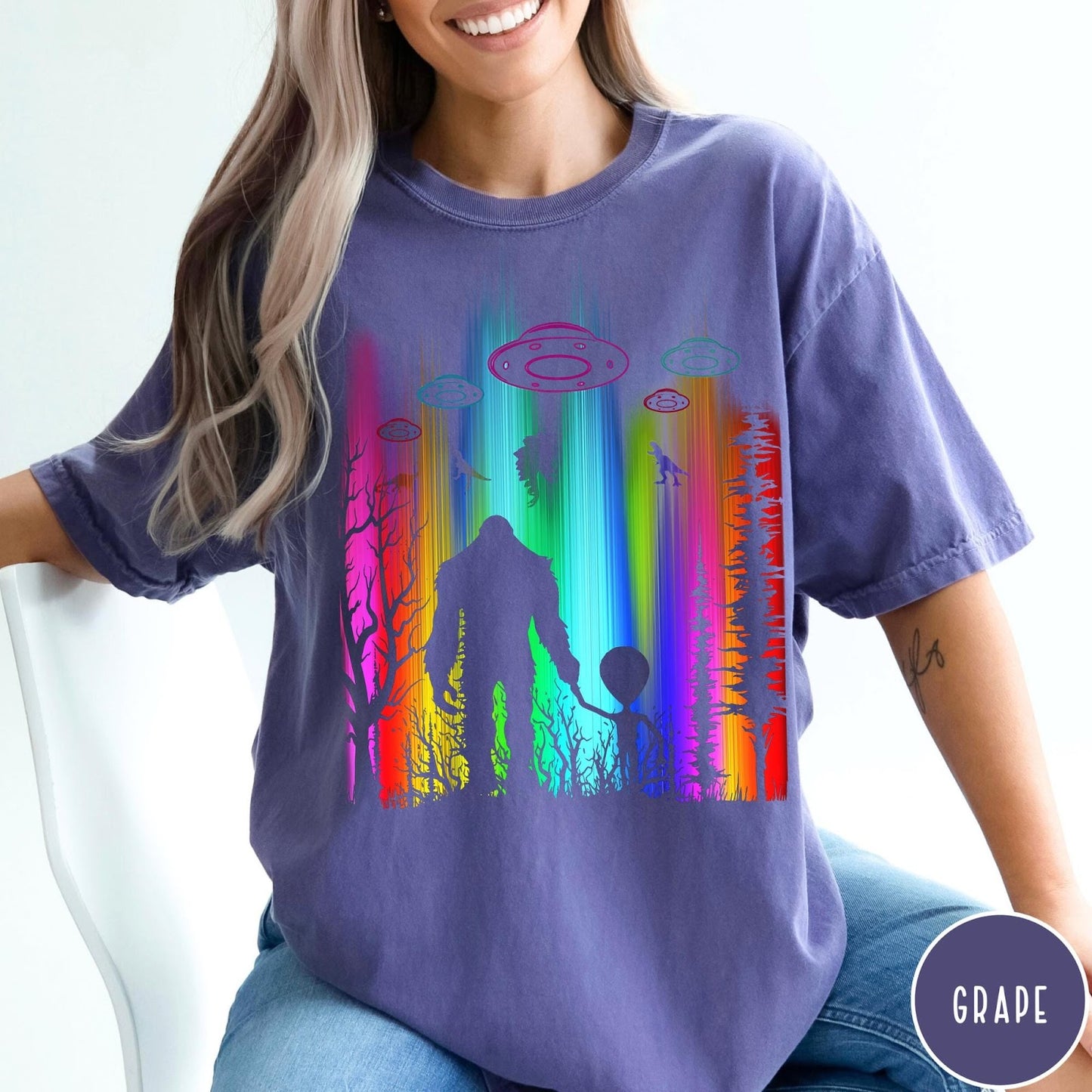 Comfort Colors tee in Grape featuring a vibrant graphic of Bigfoot and an alien holding hands in forest
