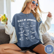 Comfort Colors tee in Blue Jean featuring illustrative style graphic with multiple seals and speech bubbles saying approval phrases