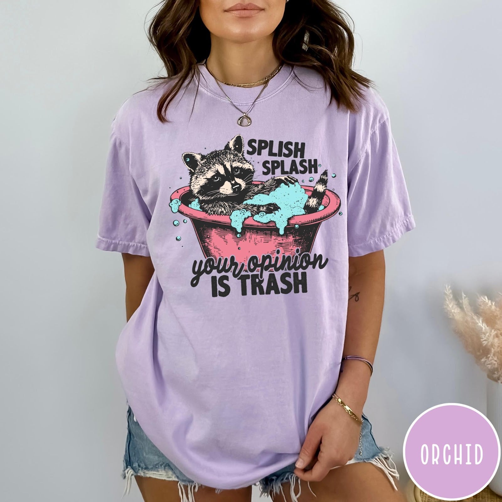 Comfort Colors tee in Orchid featuring illustrative graphic of a raccoon sitting in a pink bathtub