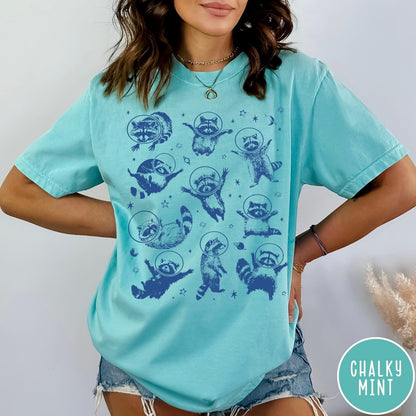 Comfort Colors tee in Chalky Mint featuring whimsical space design with multiple raccoons wearing glass astronaut helmets and stars