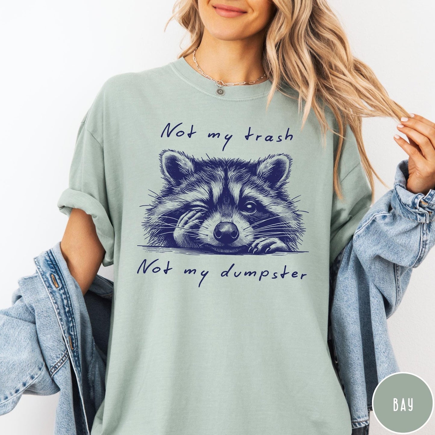 Comfort Colors tee in Bay featuring graphic illustration of a winking raccoon with text Not My Trash