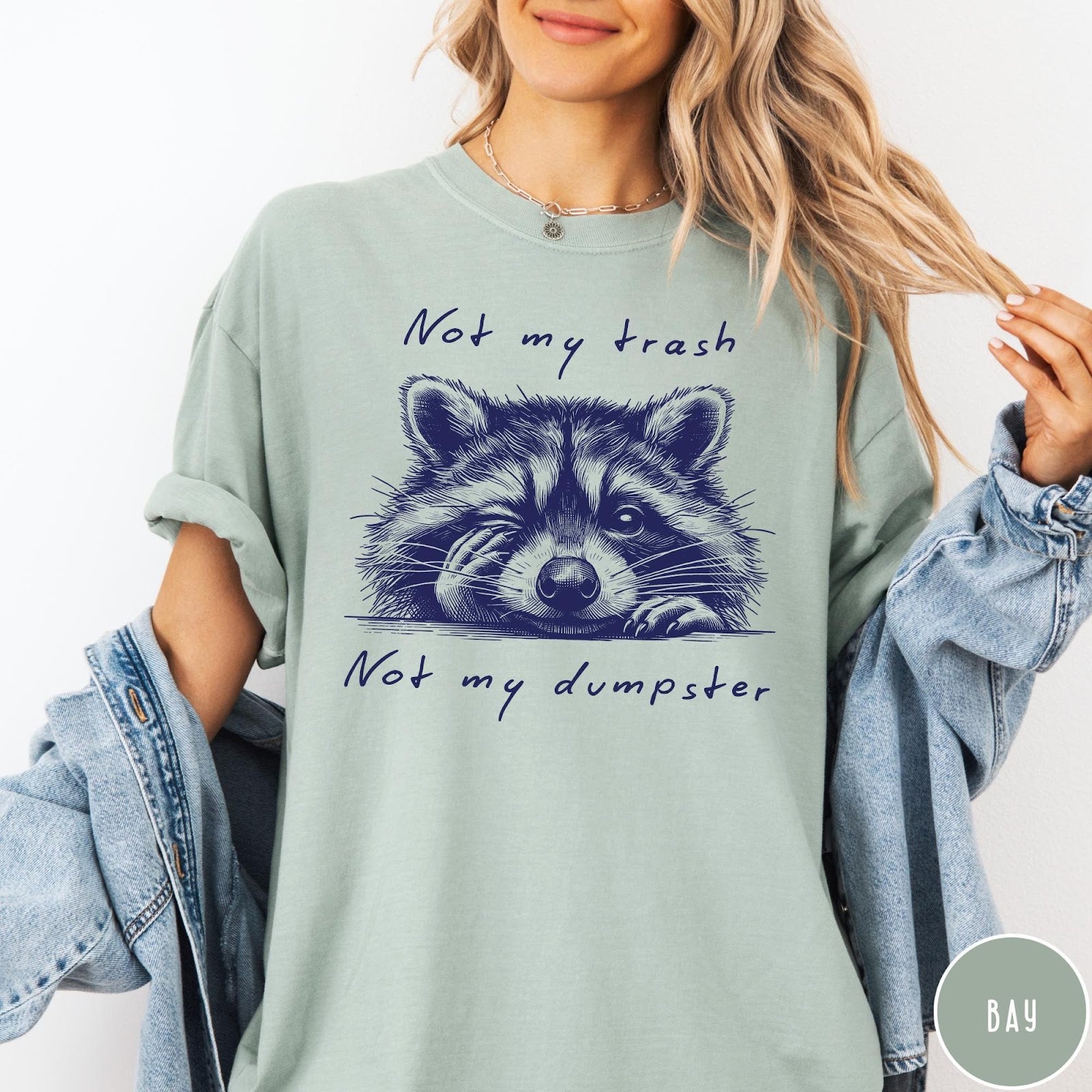 Comfort Colors tee in Bay featuring graphic illustration of a winking raccoon with text Not My Trash