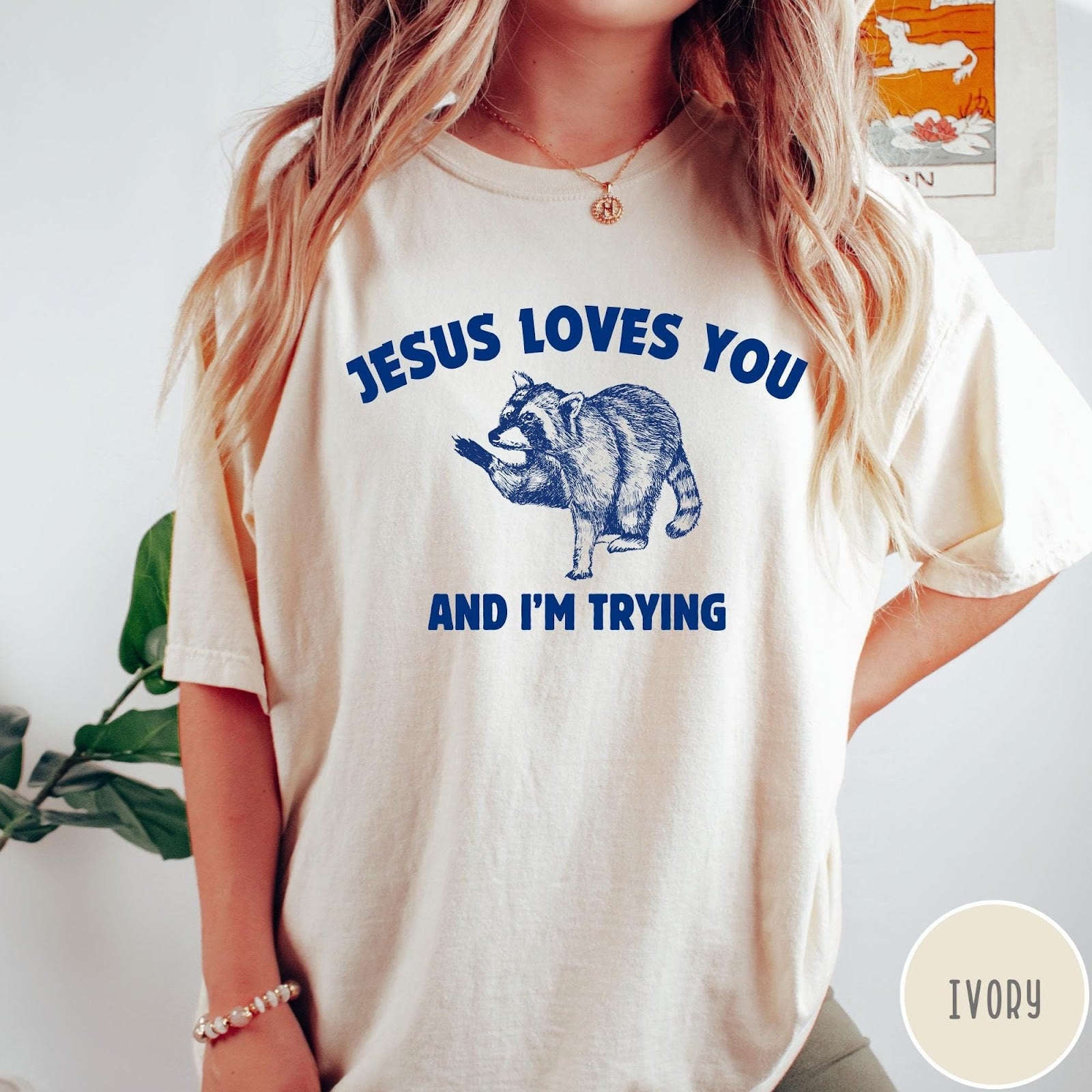 Comfort Colors tee in Ivory featuring graphic style raccoon illustration with text Jesus Loves You And I'm Trying